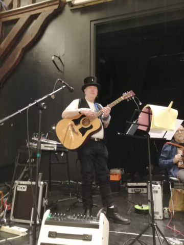 fiddler playing guitar with the ceilidh band on stage